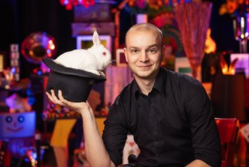 Ein Mann hält einen Hund in der Hand. In dem Hut befindet sich ein weißer Hase.