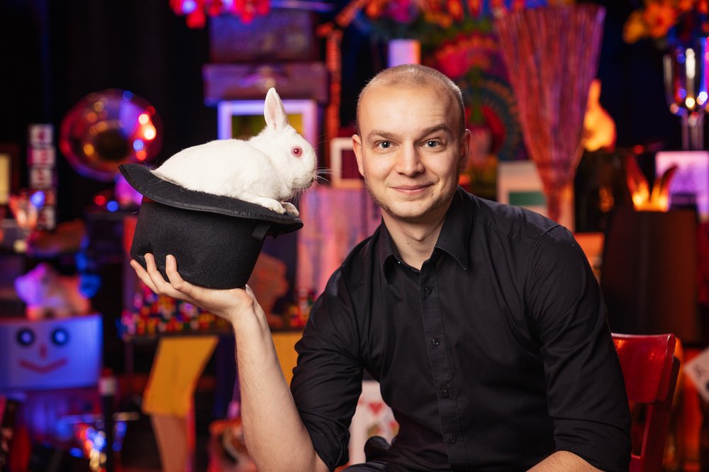 Ein Mann hält einen Hund in der Hand. In dem Hut befindet sich ein weißer Hase.
