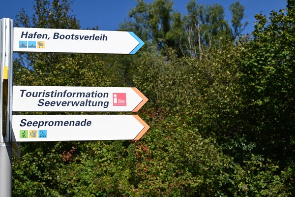 Drei Pfeilwegweiser mit den Aufschriften Hafen, Bootsverleih, Touristinformation, Seeverwaltung und Seepromenade