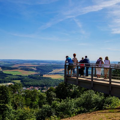 Personen stehen auf dem Aussichtssteg auf dem Schaumberg und genießen den Blick auf das Sankt Wendeler Land.