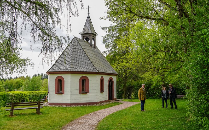 Die Peterbergkapelle steht auf dem Peterberg und besteht aus Stein. Drei Personen stehen vor dem Eingang.