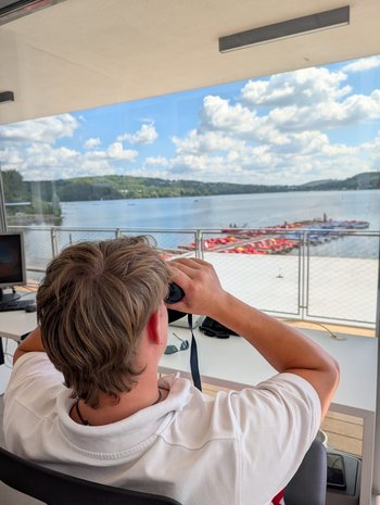 Ein Mitarbeiter der Rettungswache schaut durch ein Fernglas und beobachtet das Treiben auf dem Bostalsee.