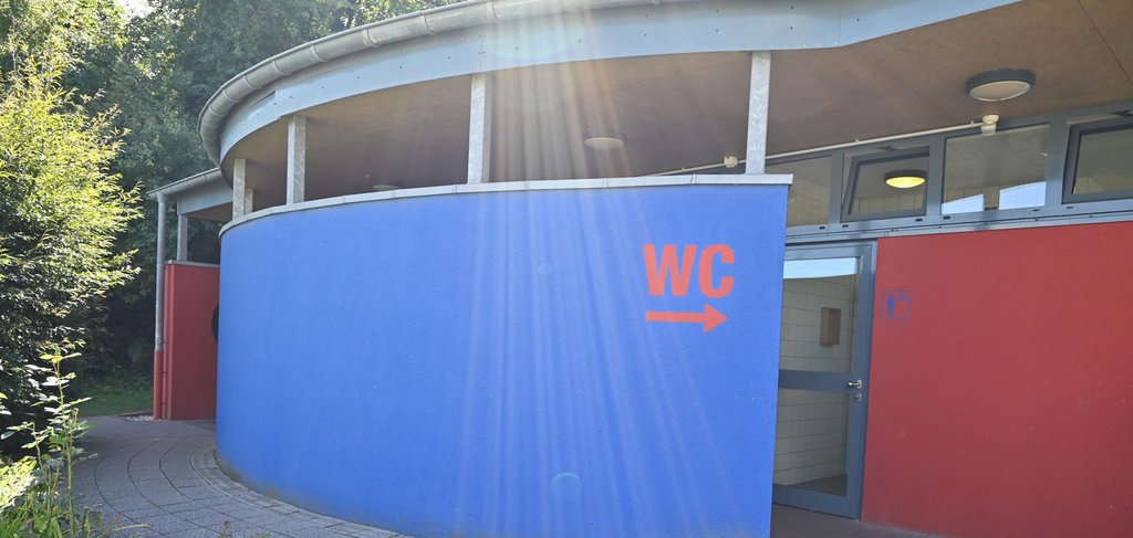 Toilettengebäude mit der Aufschrift WC und einem Pfeil nach rechts in rot auf einem blauen Hintergrund