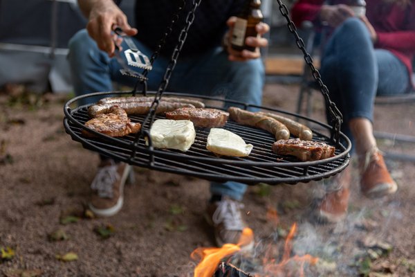2 Personen sitzen an einem Grillrost mit Grillgut darauf, wie Würstchen.