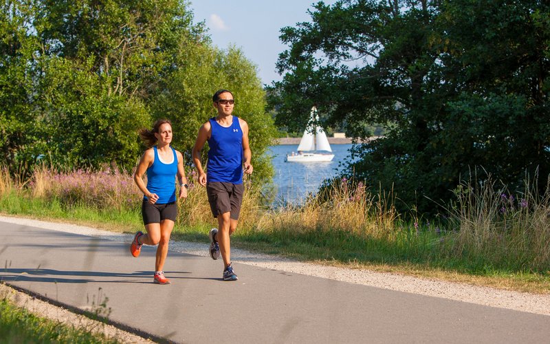 Ein Mann und eine Frau joggen auf dem Seerundweg am Wasser entlang.